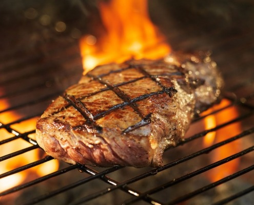 meat cooking on grill with flames