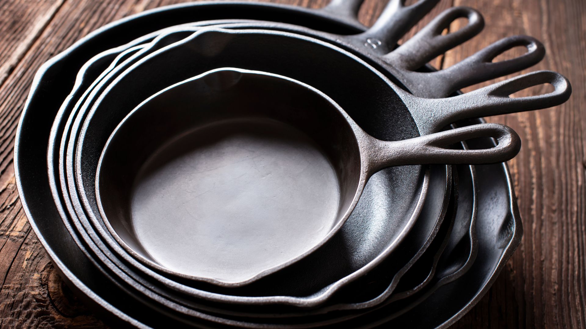 season cast iron skillets stacked together on wooden table