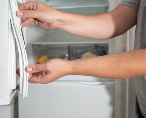 person's hands applying new seal to refrigerator door